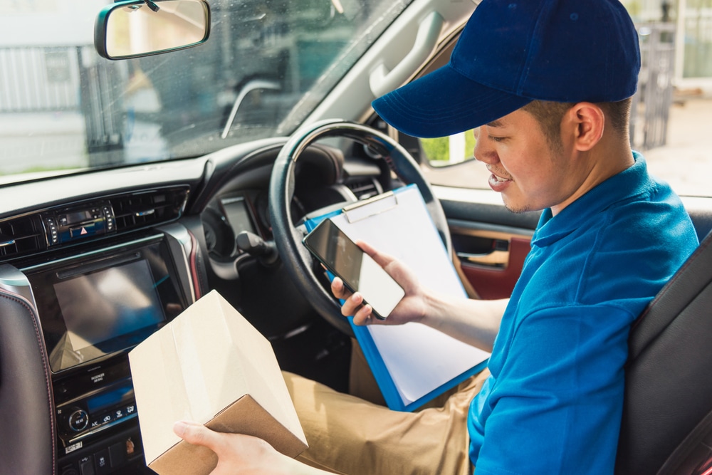 A courier holding a parcel uses his phone to plan his delivery route.